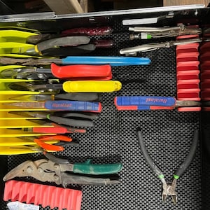 Op de afbeelding: Een geopende Craftsman-gereedschapslade met een gele kunststof organizer met diverse tangen met rode, gele, blauwe en groene handgrepen. Een rood kunststof rek houdt extra gereedschap vast, terwijl een zijkniptang op de zwarte mat ligt.