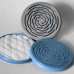 May include: Three circular components including one grey disc with a concentric slotted pattern, one blue disc with a matching concentric slotted pattern, and one blue disc containing a white, quilted, textured circular pad insert.