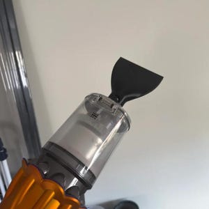 Könnte beinhalten: Ein Dyson Handstaubsauger mit einem leuchtend orangefarbenen Motorgehäuse, auf dem der Markenname in Schwarz aufgedruckt ist. Das Gerät verfügt über einen durchsichtigen Kunststoff-Staubbehälter und einen schwarzen, flachen Aufsatz.