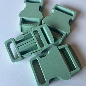 Puede incluir: Cuatro hebillas de liberación lateral de plástico verde claro. Cada hebilla tiene forma rectangular con una ranura para una correa y una sección dentada para una fijación segura. Las hebillas están diseñadas para diversas aplicaciones, como bolsos o correas.