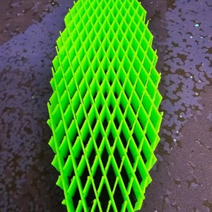 May include: A bright green, geometric lattice structure. The object is composed of a series of interconnected diamond shapes, creating an open, grid-like pattern. The object is likely 3D-printed and has a vibrant, solid color.