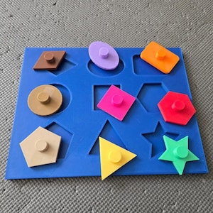 May include: A blue shape sorter toy featuring a variety of brightly coloured geometric shapes. The shapes include a brown diamond, a purple oval, an orange rectangle, a pink square, a red hexagon, a yellow triangle, and a green star.