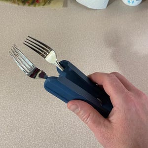 Könnte beinhalten: Ein dunkelblaues Küchenwerkzeug aus Kunststoff mit einem Klappmechanismus, das zwei Edelstahlgabeln in paralleler Position hält. Das Werkzeug hat eine matte Oberfläche und eine kompakte Struktur, wodurch die Gabeln zusammen als Zange dienen.