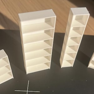 May include: Four white miniature shelving units of varying heights and widths. Each unit features multiple open horizontal shelves. The smallest unit has three shelves, the widest has five, and the two taller, narrower units have five shelves each.