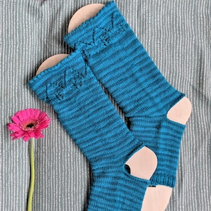 Puede incluir: Un par de calcetines de punto azul turquesa con un patrón a rayas y un diseño de punto decorativo. Los calcetines están sobre un bloque de madera.