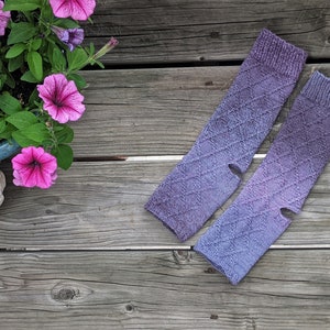 Puede incluir: Un par de calentadores de brazo de punto morado y azul con un patrón de diamante. Los calentadores de brazo tienen un agujero para el pulgar a cada lado.