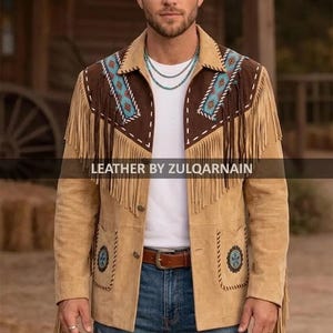 Puede incluir: Chaqueta de ante color canela con detalles marrones, flecos y bordados turquesa y blancos. La chaqueta tiene cuello, bolsillos y cierre de botones. El texto "LEATHER BY ZULQARNAIN" es visible.