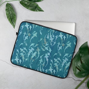 May include: A teal blue laptop sleeve with a pattern of white shark silhouettes. The sleeve has a black zipper and a black border.