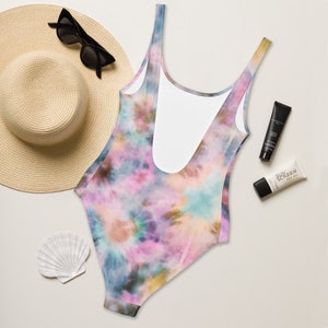 May include: A tie-dye swimsuit with a pink, blue, and brown color scheme. The swimsuit has a scoop neck and a low back.
