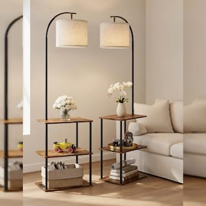 May include: Two floor lamps with integrated three-tier wooden shelves and black metal frames. Each lamp features a cylindrical beige fabric shade. The shelves hold decorative items including a flower vase, a toy car, books, and a basket.