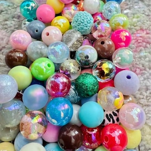 May include: A collection of assorted round beads in various colours, textures, and finishes. The beads include solid, translucent, glittery, iridescent, and patterned styles, featuring shades of pink, blue, green, yellow, brown, and white.