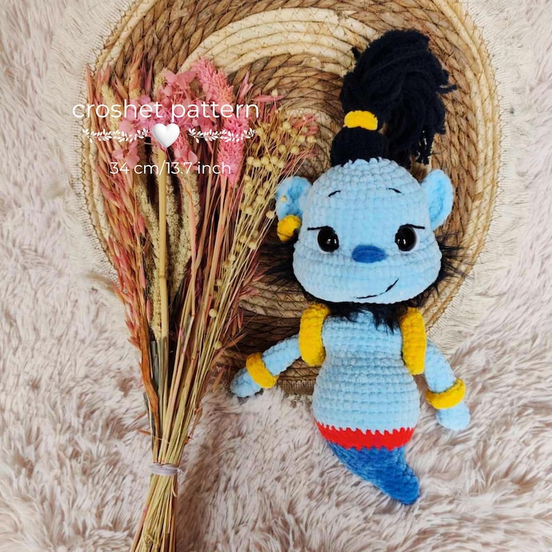 May include: A handmade blue crochet genie doll with black hair and yellow accents. The doll is approximately 13.7 inches (34 cm) tall. The image also includes a bouquet of dried flowers and the text "crochet pattern".