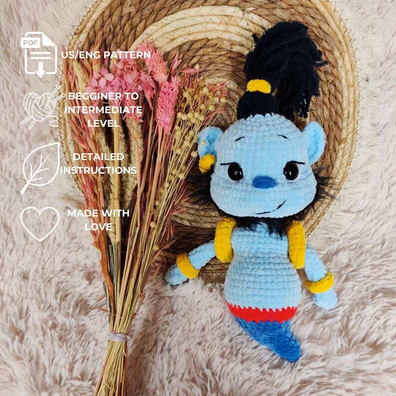 May include: A handmade blue crochet genie doll with yellow accents and a black ponytail. The doll has a red and blue tail and is next to a bundle of dried pink flowers. Text on the image reads "US/ENG PATTERN", "BEGINNER TO INTERMEDIATE LEVEL", "DETAILED INSTRUCTIONS", and "MADE WITH LOVE".