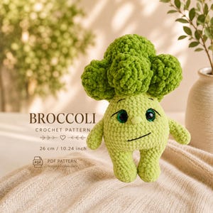 K&ouml;nnte beinhalten: Ein geh&auml;keltes Brokkoli-Pl&uuml;schtier mit einem l&auml;chelnden Gesicht, Armen und Beinen. Der Brokkolikopf ist leuchtend gr&uuml;n und der K&ouml;rper ist hellgr&uuml;n. Der Text "BROCCOLI CROCHET PATTERN" ist zu sehen. Das Spielzeug ist 26 cm gro&szlig;.