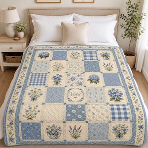 May include: A patchwork quilt featuring a grid of squares with blue and cream floral patterns, gingham checks, and botanical illustrations. One central square displays the name Violet in cursive script surrounded by a floral wreath border.