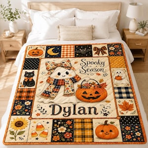 May include: A quilted throw blanket featuring a patchwork design with orange, black, and cream colors. The center displays a ghost wearing a floral scarf and bow, holding a pumpkin basket, with the text Spooky Season and the name Dylan.