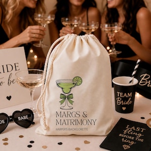 May include: A cream-coloured drawstring bag featuring a margarita graphic and the text "MARGS & MATRIMONY HARPER'S BACHELORETTE." The bag is part of a bachelorette party theme, with other party supplies visible.