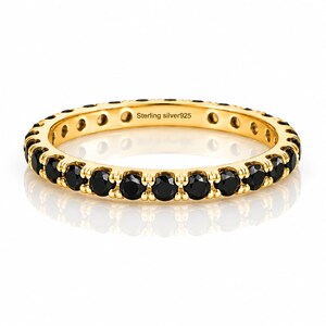 Könnte beinhalten: Ein goldfarbener Eternity-Ring mit einer durchgehenden Reihe runder schwarzer Steine, die in ein Metallband gefasst sind. Die Innenseite des Rings ist mit dem Text sterling silver925 graviert, was auf das Metallmaterial dieses Schmuckstücks hinweist.