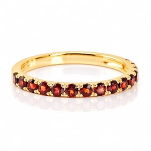 Op de afbeelding: Een gouden ring met een doorlopende rij kleine, ronde, dieprode granaat edelstenen in een gedeelde klauwzetting. Het metaal heeft een gepolijste, reflecterende afwerking en de stenen zijn gelijkmatig verdeeld over de voorzijde van de ringband.