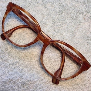 May include: Brown tortoiseshell eyeglasses with a rounded frame shape. The inner temple arm features the text BURBERRY MADE IN ITALY, while the other arm displays the measurements 52-17 140. The frames are constructed from a glossy acetate material.