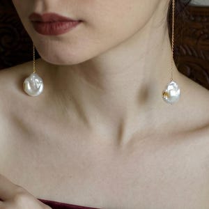 May include: Elegant gold chain earrings with large, irregular white pearls. The pearls have a lustrous sheen and hang delicately from the earlobes. The earrings are a classic accessory, suitable for formal or casual wear.