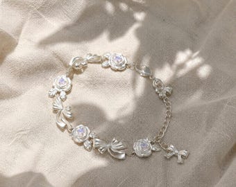 Pulsera de rosa y lazo de plata: delicada joya floral coqueta para mujer.