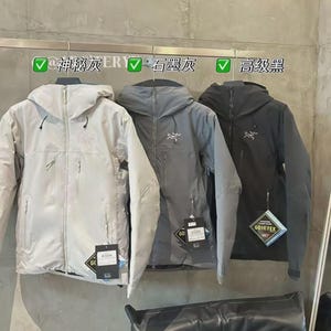 May include: Three hooded jackets in light grey, grey, and dark grey hang on a rack. Each jacket has a zipper closure and a small logo on the chest. The jackets have tags with the text "GORE-TEX". The text above the jackets reads "@Mysterious Grey ER", "Graphite Grey", and "High-end Black".