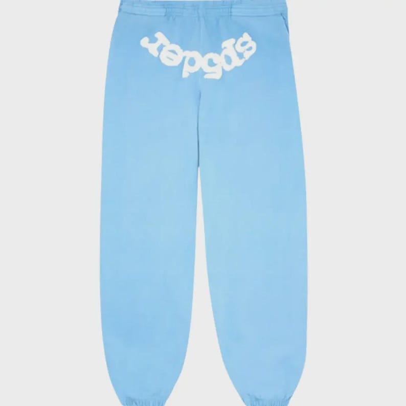 Op de afbeelding: Lichtblauwe joggingbroek met het woord "spider" in het wit, gebogen over de achterkant. De broek heeft een relaxte pasvorm en een taille met trekkoord. De stof lijkt een lichtgewicht materiaal te zijn.