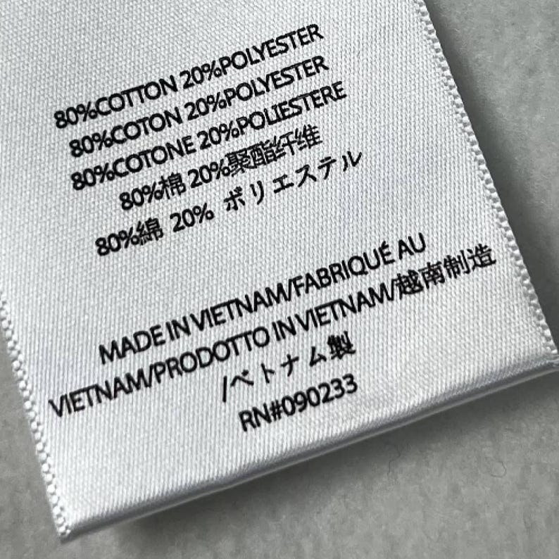 Puede incluir: Primer plano de una etiqueta de tela blanca con texto negro. La etiqueta indica la composici&oacute;n de la tela: 80% algod&oacute;n y 20% poli&eacute;ster en varios idiomas. Tambi&eacute;n indica 'Hecho en Vietnam'. RN #090233.
