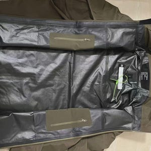 May include: Olive green waterproof jacket with a black interior. The jacket features two zipped pockets on the inside and a tag with the brand name. The jacket is designed for outdoor activities and protection from the elements.