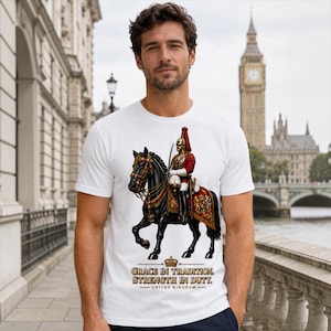 May include: A white short-sleeved t-shirt featuring a graphic of a British cavalry soldier in a red uniform riding a black horse. Below the graphic, the text reads: GRACE IN TRADITION. STRENGTH IN DUTY. UNITED KINGDOM, with a small crown icon above.