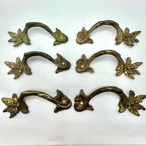 May include: Six antique brass drawer pulls with a floral design. Each pull has a curved handle and decorative ends. The brass has a vintage patina, adding to the aged aesthetic. These pulls are suitable for furniture restoration or decorative projects.
