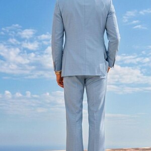May include: A light blue suit, including a blazer and trousers, is shown from the back against a blue sky with clouds. The suit is tailored and has a classic design. The text "IMPERIAL ATTIRE - TAILORED TO ELEVATE" is visible at the top.