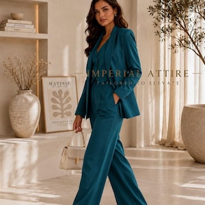 K&ouml;nnte beinhalten: Ein dreiteiliger Anzug in Petrol, bestehend aus einem Blazer, einer Weste und einer Hose mit weitem Bein. Der Blazer hat ein fallendes Revers und lange &Auml;rmel. Die Weste ist gekn&ouml;pft und die Hose hat eine hohe Taille. Der Text IMPERIAL ATTIRE TAILORED TO ELEVATE ist sichtbar.