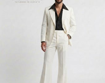 May include: A cream-colored suit with wide-leg pants and a black shirt. The suit jacket has a wide lapel. The text "IMPERIAL ATTIRE - TAILORED TO ELEVATE" is at the top. The person is wearing a gold chain and a watch.