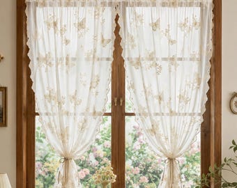 May include: A pair of sheer white curtains featuring an embroidered butterfly pattern and scalloped edges. The curtains are gathered at the centre with ties and hang from a wooden window frame, allowing light to pass through the translucent fabric.