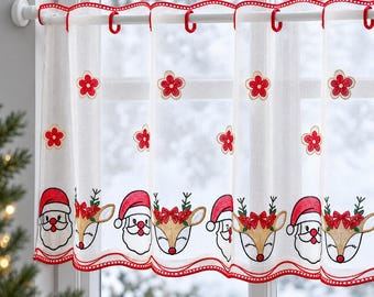 Puede incluir: Una cortina de café blanca y transparente con un patrón repetitivo de flores rojas bordadas y un borde inferior que alterna caras de Papá Noel y cabezas de reno con lazos rojos, acabado con un borde festoneado en rojo.