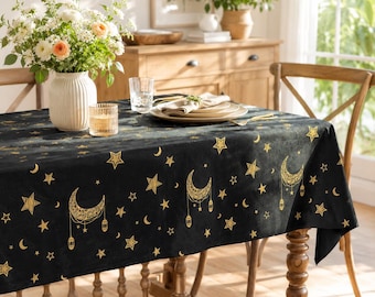 Puede incluir: Un mantel rectangular negro con un patrón repetitivo de lámina dorada que muestra lunas crecientes, linternas colgantes y estrellas de varios tamaños. La tela cubre una mesa de madera, creando un contraste oscuro en la habitación.