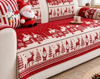Puede incluir: Un sofá de color crema cubierto con un camino de tela rojo y blanco con un patrón repetitivo de casas, renos, pinos y gnomos. Un muñeco de peluche de Santa Claus está sentado en el sofá junto a un cojín a rayas con un gráfico de perro.