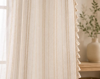 Puede incluir: Un panel de cortina de color beige claro con rayas verticales de color tostado y un borde decorativo adornado con una serie de pequeñas borlas de tela colgantes. La tela tiene un aspecto tejido y texturizado que permite el paso de la luz.