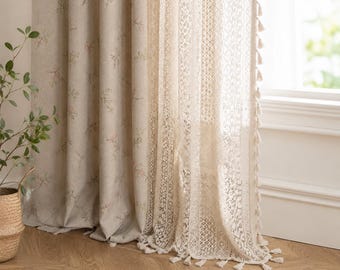 May include: A pair of curtains featuring a beige fabric panel with a delicate floral pattern and a sheer white lace panel with intricate geometric designs. The lace panel is finished with a decorative fringe of small tassels along the edge.