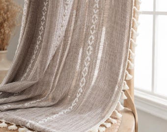 May include: A taupe-coloured fabric curtain featuring vertical white embroidered geometric patterns and stripes. The edge of the curtain is finished with a row of small, white decorative tassels that hang along the side and bottom hem.