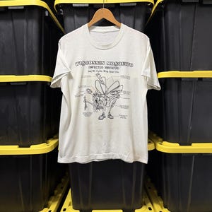 May include: A white short-sleeve t-shirt featuring a black graphic of a Wisconsin Mosquito with the text "WISCONSIN MOSQUITO (INFECTUS IRRITATUS) Avg. Wt. 0.68 kg. Wing Span 30.48 cm" and various labels pointing to parts of the insect illustration.