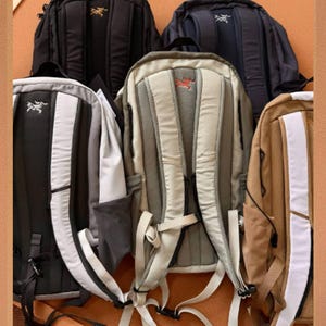 May include: A collection of backpacks in various colors, including black, navy, and tan. Each backpack features a padded back panel, adjustable straps, and a logo. The backpacks are designed for outdoor activities and travel.