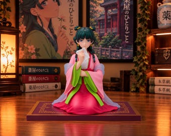 May include: A collectible anime-style figurine of a character with dark teal hair styled in buns, wearing a vibrant pink and green traditional-style robe. The figure is kneeling on a rectangular purple base, holding a small white paper in their hands.