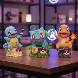 Puede incluir: Tres figuras de personajes Pokémon que incluyen a Squirtle sobre una base de arena con una pala, Bulbasaur sobre una base de hierba con un girasol y Charmander sobre una base rocosa con una llama, cada una con una Poké Ball roja y blanca.