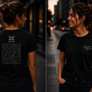 Op de afbeelding: Een zwart T-shirt met korte mouwen, voorzien van een kleine afbeelding en een grote QR-code met de tekst SCAN ME op de achterkant. De voorkant van het shirt toont de tekst PROJECT BLU in witte letters met een klein rond icoon ertussen.