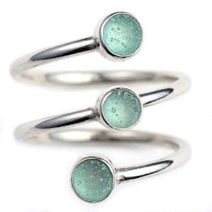 May include: A silver-toned spiral ring featuring three circular, light seafoam green cabochons. Each cabochon has a textured, bubbly surface set within a smooth metal bezel. The ring wraps around in a continuous coil design with a polished finish.
