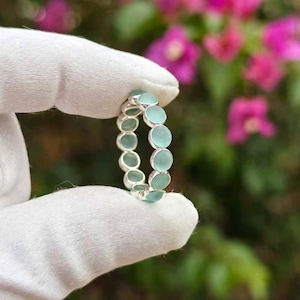 Peut inclure: Une bague en argent composée d'une bande continue de petites pierres cabochons rondes bleu-vert clair. Les pierres sont serties dans une monture métallique, créant un motif circulaire uniforme qui entoure toute la circonférence du bijou.