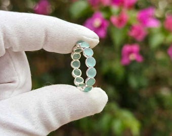 May include: A silver ring featuring a continuous band of small, round, light blue-green cabochon stones. The stones are set in a metallic frame, creating a uniform circular design that encircles the entire circumference of the jewelry piece.